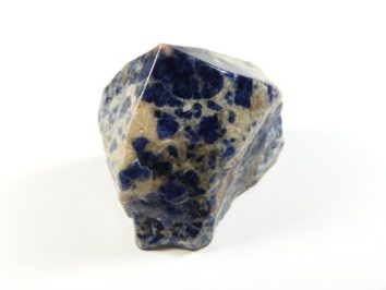 Sodalit kamień ozdobny do dekoracji, częściowo gładzony, częściowo naturalny. Niebiesko-biały minerał sodalit na białym tle, widoczna nieregularna powierzchnia.