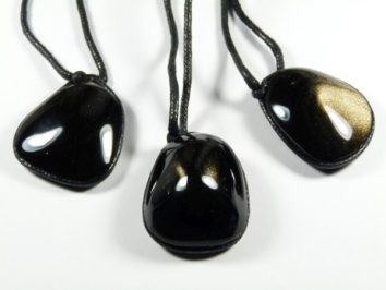 Trzy czarne kamienie obsydianu na sznurkach, ułożone na białym tle.