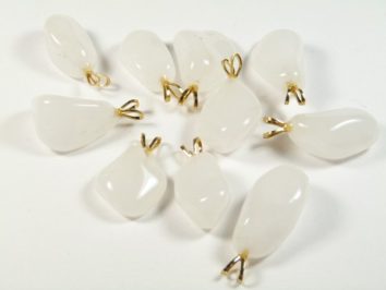 Białe kamienie z zawieszkami leżące na białym tle, przygotowane do wyrobu biżuterii.