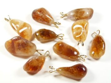 Dziesięć bursztynowych zawieszek na biżuterię, ułożonych na białym tle.