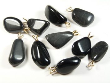 Czarne kamienie szlifowane z metalowymi zawieszkami, ułożone na białym tle.