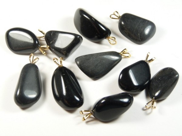 Czarne kamienie szlifowane z metalowymi zawieszkami, ułożone na białym tle.