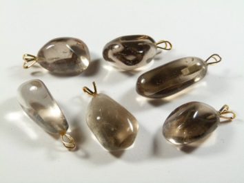 Sześć przezroczystych, brązowych kamieni z zawieszkami na białym tle.
