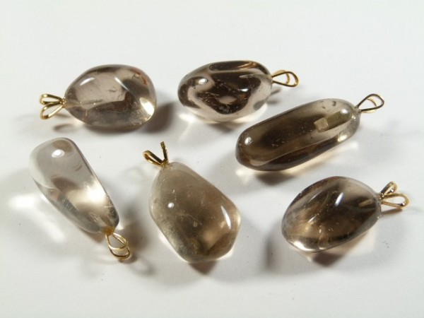 Sześć przezroczystych, brązowych kamieni z zawieszkami na białym tle.
