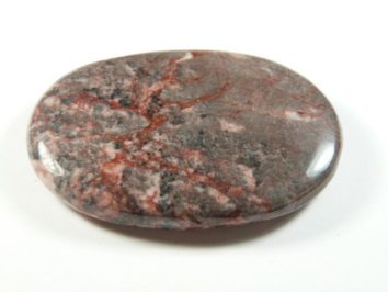 Jaspis zebra różowy - kamień gładzony, polerowany, szlifowany. Wypolerowany, owalny kamień z czerwonymi i szarymi żyłkami na białym tle.