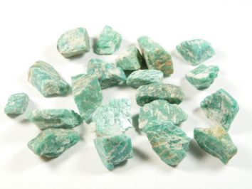 Zielone, nieobrobione kawałki minerału amazonit leżące na białym tle.