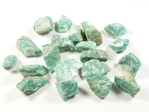 Zielone, nieobrobione kawałki minerału amazonit leżące na białym tle.