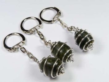 Werdyt gładzony w spirali - breloczek. Trzy breloczki z ozdobnymi kamieniami owiniętymi srebrnym drutem, leżące na białym tle.