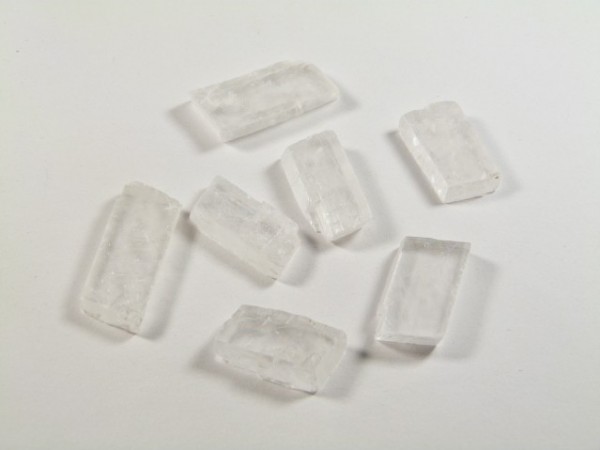 Spar islandzki - kamień naturalny, surowy, nieszlifowany. Siedem białych kryształków na białym tle, ułożonych w nieregularny sposób.