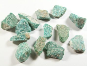 Kilka nieregularnych kawałków zielonego minerału amazonitu na białym tle.