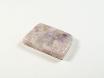 Prostokątny, polerowany kamień o jasnofioletowym zabarwieniu na białym tle.