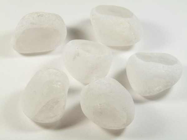 Sześć białych, matowych kamyków leży na białym tle.