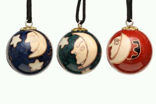 Trzy kolorowe bombki z motywem księżyca i gwiazd zawieszone na czarnych sznurkach.