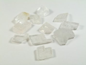 Spar islandzki - kamień naturalny, surowy, nieszlifowany. Kilka przezroczystych kryształków na białym tle.