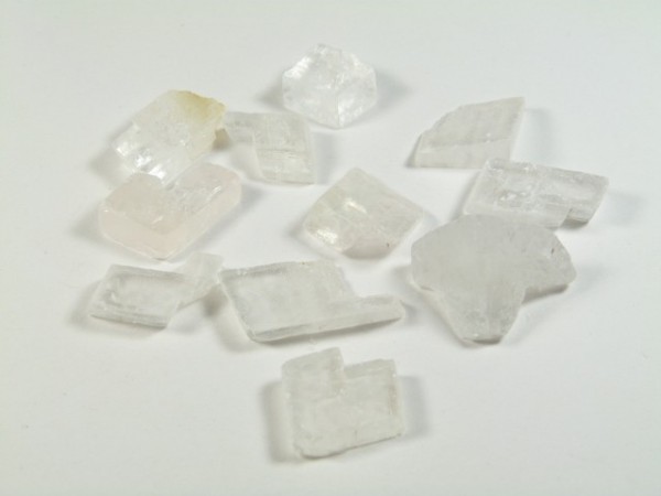 Spar islandzki - kamień naturalny, surowy, nieszlifowany. Kilka przezroczystych kryształków na białym tle.