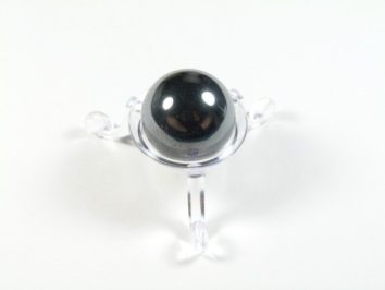 Kula hematyt szlifowany średnica 2,5 cm. Podstawka trónożna z kulistym, czarnym kamieniem na białym tle.