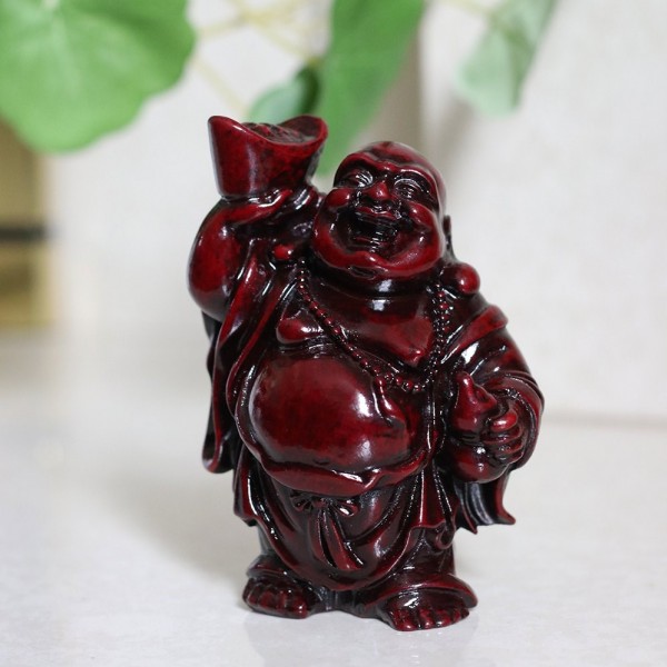 Czerwona figurka śmiejącego się Buddy trzymającego złoty sztabek w jednej ręce.