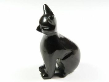 Czarna, błyszcząca figurka kota siedzącego na białym tle.