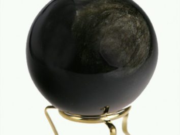 Czarna kula do wróżenia ustawiona na złotym stojaku, na jasnym tle.