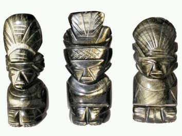 Trzy kamienne figurki przedstawiające postacie z indiańskimi pióropuszami ustawione obok siebie.