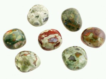 Riolit - kamień gładzony, polerowany, szlifowany i bębnowany w formie otoczaka. Siedem polerowanych, wielobarwnych kamieni na jasnym tle.