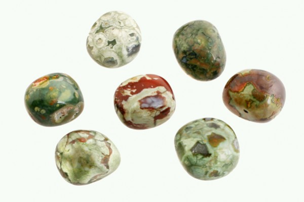 Riolit - kamień gładzony, polerowany, szlifowany i bębnowany w formie otoczaka. Siedem polerowanych, wielobarwnych kamieni na jasnym tle.
