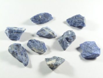 Nieoszlifowane niebieskie kamienie sodalitu ułożone na białym tle.