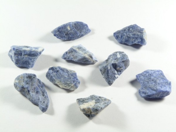 Nieoszlifowane niebieskie kamienie sodalitu ułożone na białym tle.