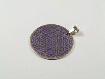 Okrągły wisiorek z wzorem kwiatu życia na fioletowym tle, leżący na białym podłożu.
