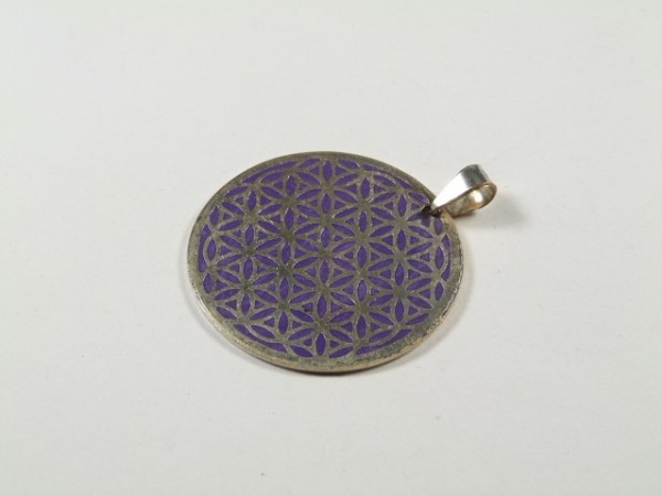 Okrągły wisiorek z wzorem kwiatu życia na fioletowym tle, leżący na białym podłożu.