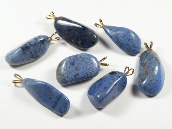 Siedem niebieskich kamieni z zawieszkami na białym tle, ułożonych w rozproszeniu.