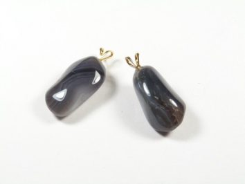 Dwa ciemne, gładkie kamienie z zawieszkami na białym tle.