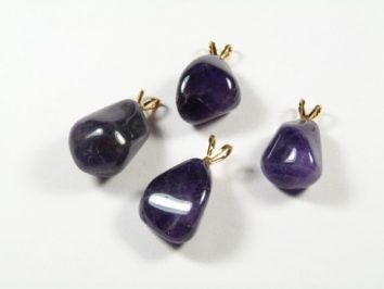Cztery fioletowe kamienie półszlachetne z zawieszkami, leżące na białym tle.