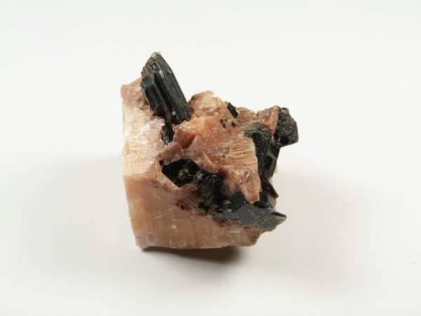 Różowy minerał z czarnymi kryształami, sfotografowany na białym tle.