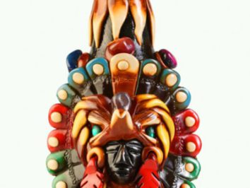 Kolorowa figurka przedstawiająca postać w pióropuszu inspirowanym kulturą aztecką.