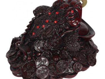 Figurka żaby trzymającej monetę w pysku, siedzącej na stosie chińskich monet.