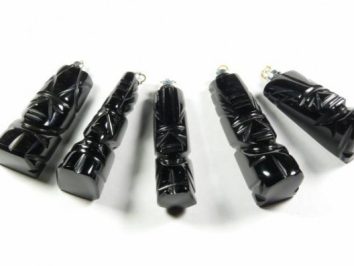 Pięć czarnych wisiorków w kształcie totemów leży na białym tle.