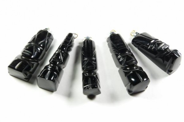 Pięć czarnych wisiorków w kształcie totemów leży na białym tle.