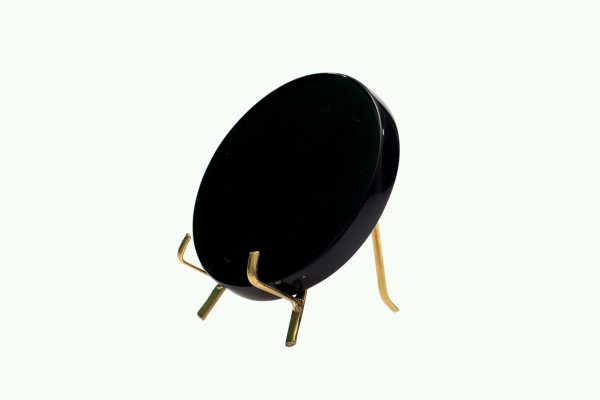 Czarny, okrągły przedmiot na złotym stojaku na jasnym tle.