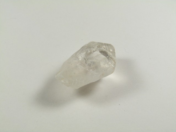 Przezroczysty kryształ kwarcu leżący na białym tle.