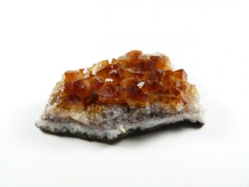 Fragment minerału cytrynu z widocznymi pomarańczowymi kryształami na białym tle.