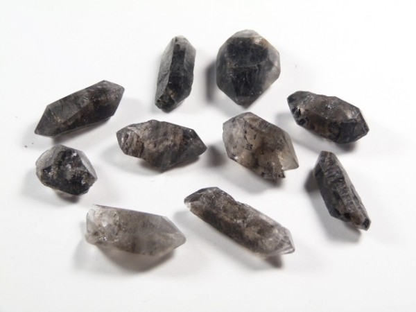 Kwarc tybetański - kamień naturalny, surowy, nieszlifowany. Kilka ciemnoszarych kryształów kwarcu leży na białym tle.