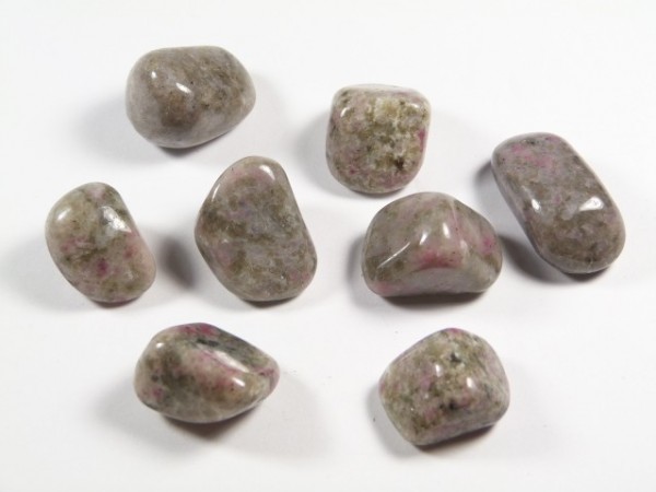 Osiem wypolerowanych kamieni o szaro-różowym zabarwieniu ułożonych na białym tle.