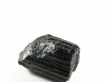 Czarny turmalin - kamień naturalny, surowy, nieszlifowany. Czarny, błyszczący kryształ turmalinu na białym tle.