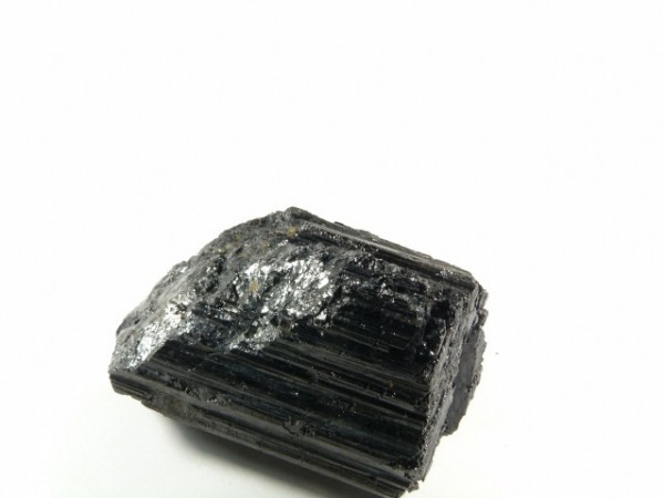 Czarny turmalin - kamień naturalny, surowy, nieszlifowany. Czarny, błyszczący kryształ turmalinu na białym tle.