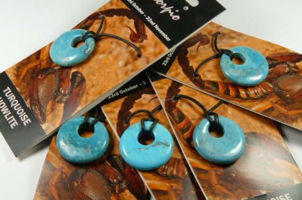 Pięć turkusowych zawieszek na czarnych sznurkach, ułożonych na kartach z wizerunkiem skorpiona.