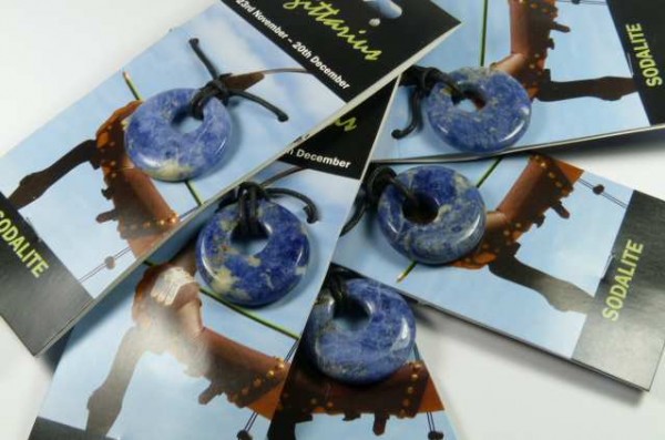 Pięć granatowych wisiorków z sodalitu na czarnych sznurkach, ułożonych na kartonikach.