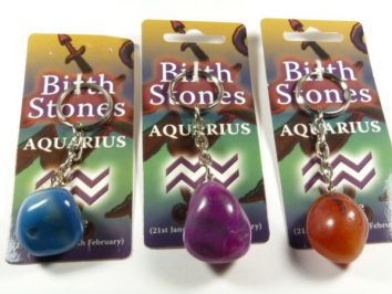 Trzy breloki z kolorowymi kamieniami na kartach z napisem "Birth Stones Aquarius".