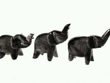 Trzy czarne figurki słoni stojące w rzędzie na białym tle.