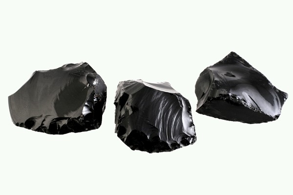 Trzy czarne bryły obsydianu na jasnym tle.